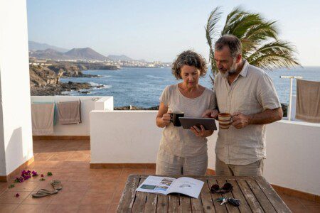 Ein Paar sitzt entspannt auf der Terrasse und stöbert gemeinsam nach passenden Ferienunterkünften.